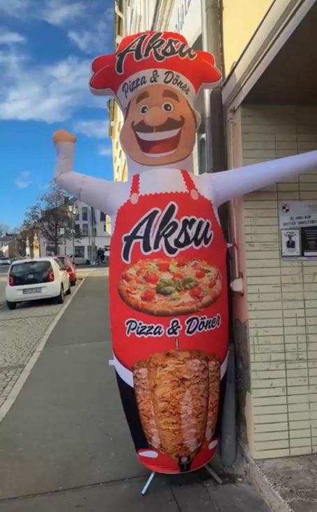 Luftfigur eines Kochs mit Pizza- und Kebabsymbolen vor einem Restaurant.